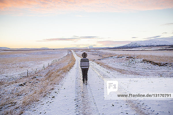 Woman walking on snow-covered country road  Iceland