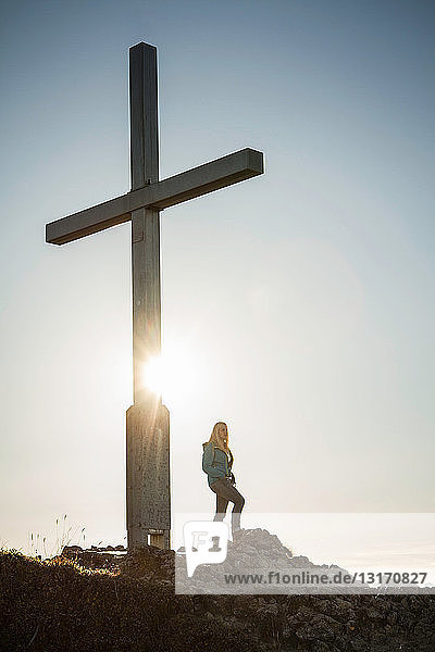 Wanderer steht am Kreuz auf felsiger Bergkuppe