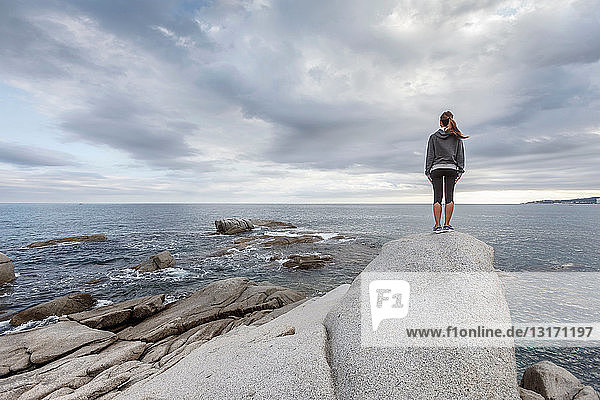 Frau auf Felsbrocken mit Blick auf den Ozean