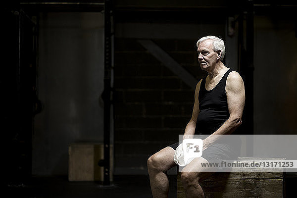 Älterer Mann sitzt ausruhend in dunkler Turnhalle
