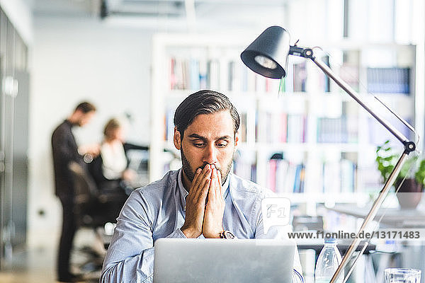Tensed businessman covering mouth while looking at laptop in office