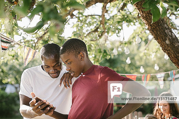 Vater und Sohn schauen während der Gartenparty im Garten auf das Handy