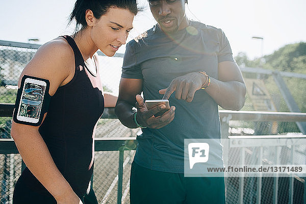 Sportler zeigt einer Sportlerin ein Mobiltelefon  während er am Geländer auf der Brücke steht