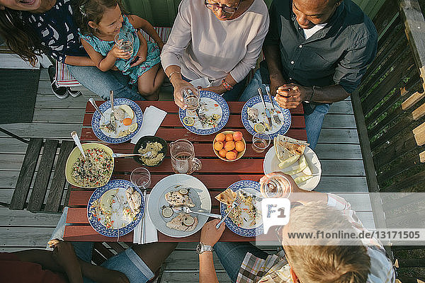 Hochwinkelaufnahme einer Mehrgenerationen-Familie beim Mittagessen am Tisch auf der Veranda