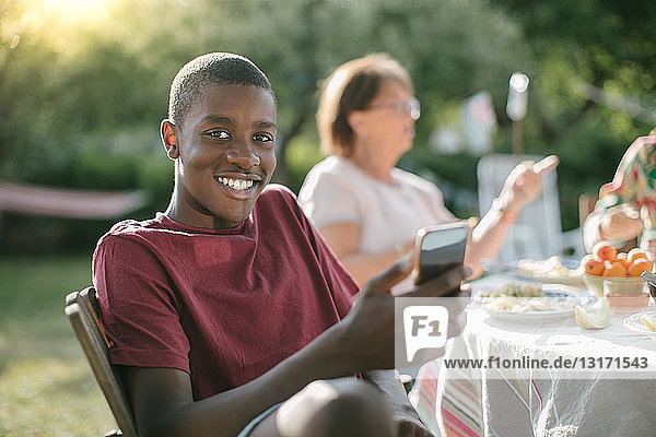 Portrait of smiling boy using mobile phone in backyard during garden party