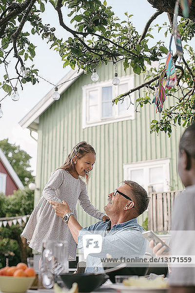 Playful girl standing by grandfather in backyard during garden party