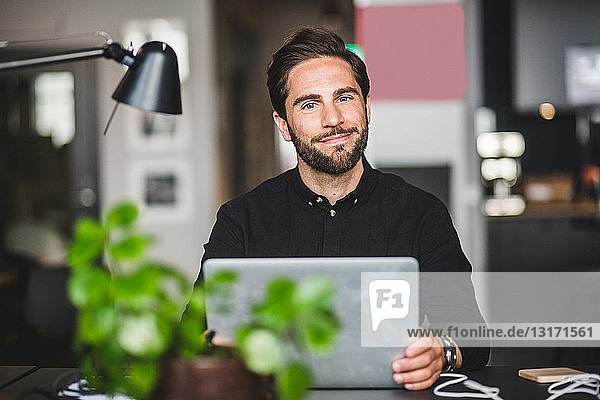 Portrait of confident creative businessman sitting at desk in office