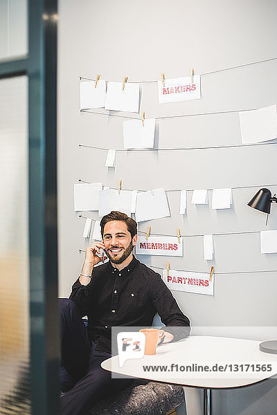 Kreativer Geschäftsmann lächelt beim Telefonieren mit dem Handy am Schreibtisch im Büro