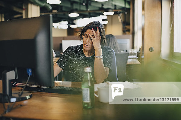 Müde Geschäftsfrau mit dem Kopf in der Hand am Computerschreibtisch im Büro sitzend