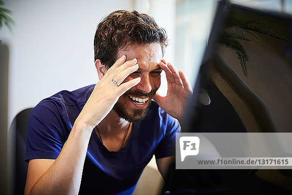 Cheerful businessman looking at computer monitor while sitting in creative office