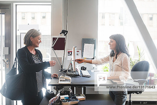 Geschäftsfrau gibt Unternehmerin Karte am Schalter im Büro
