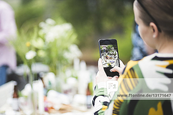 Cropped image of woman photographing dining table through mobile phone in backyard