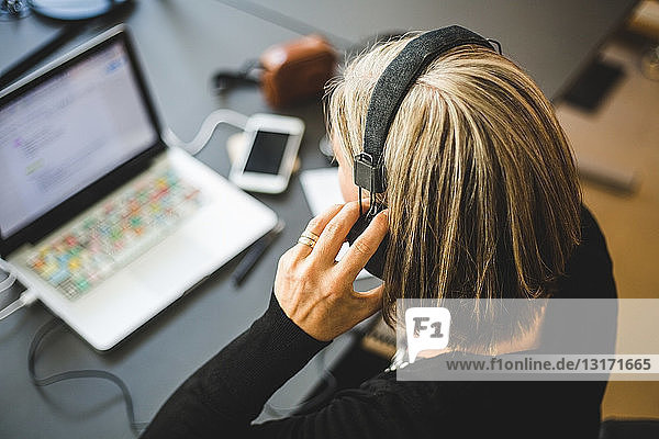 Businesswoman listening through headphones while using laptop at desk in office