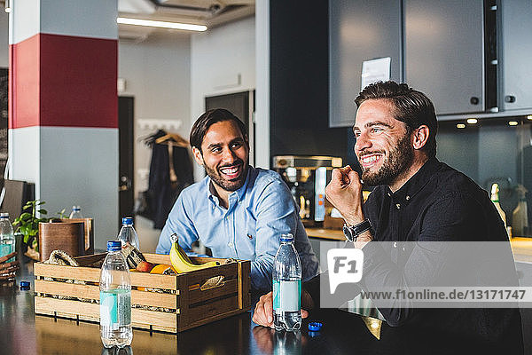 Male colleagues smiling while sitting at table in office
