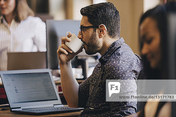 Mittlerer erwachsener Geschäftsmann trinkt Kaffee mit Laptop auf dem Schreibtisch im Büro