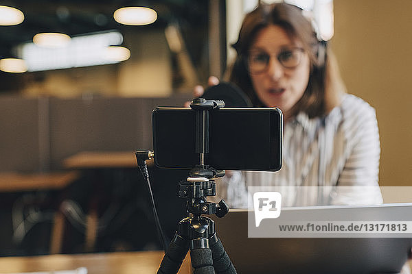 Smart phone on tripod filming businesswoman with laptop in office