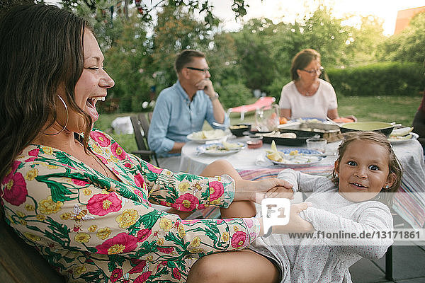 Cheerful mother holding hands of daughter while sitting on chair during garden party