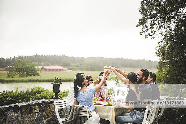 Männliche und weibliche Freunde stoßen während der Dinnerparty im Hinterhof auf Getränke an
