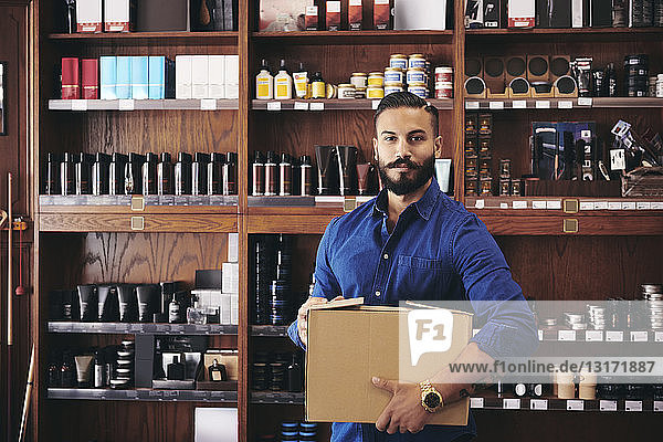 Porträt eines selbstbewussten Verkäufers  der eine Kiste trägt  während er im Feinkostladen vor dem Regal steht