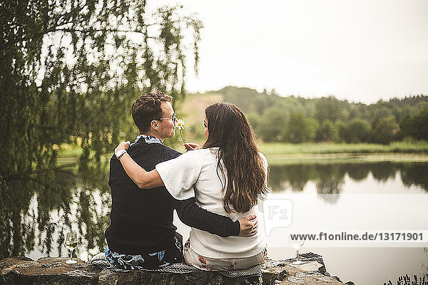 Rear view of romantic couple sitting on retaining wall against lake