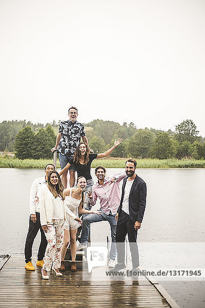Portrait of cheerful multi-ethic friends standing on jetty over lake during holiday
