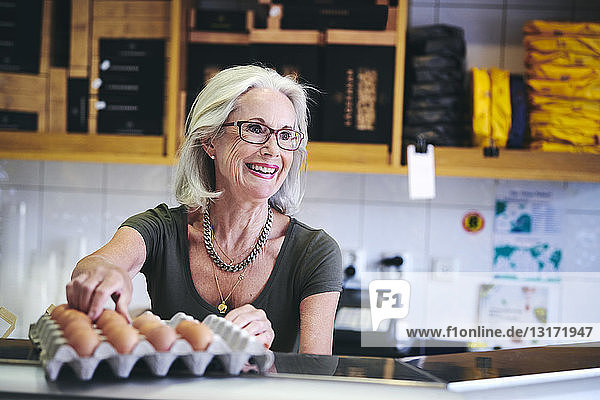 Verkaufsleiterin lächelt beim Pflücken von braunen Eiern aus dem Karton im Feinkostladen