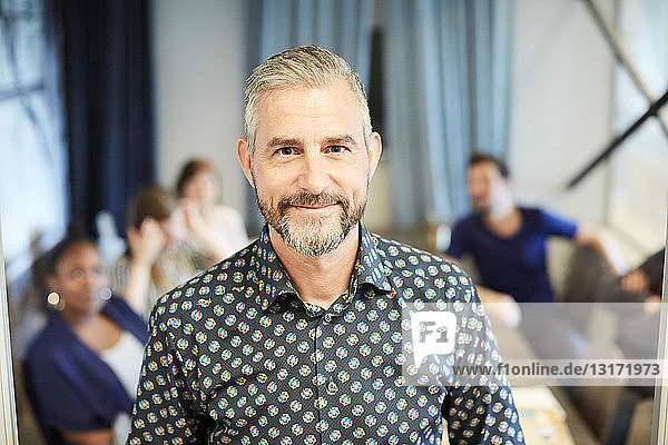 Portrait of confident mature businessman standing while colleagues in background at office