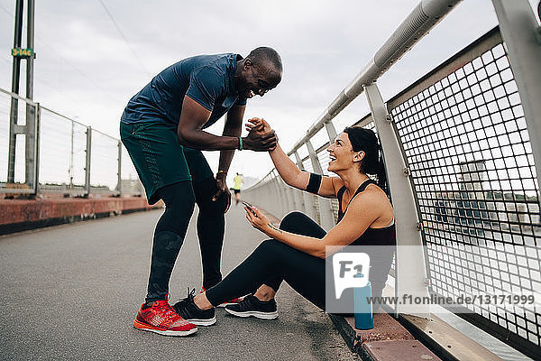 Cheerful male and female athletes holding hands during sports training on footbridge