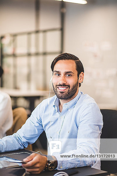 Porträt eines selbstbewussten  kreativen Geschäftsmannes  der In-Ear-Kopfhörer benutzt  während er im Büro am Schreibtisch sitzt