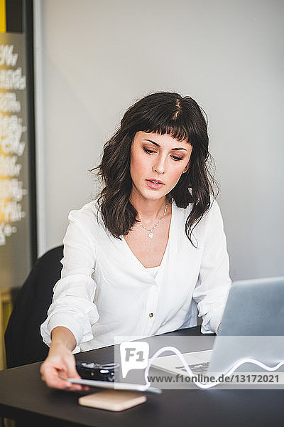 Kreative Geschäftsfrau benutzt Mobiltelefon  während sie im Büro am Schreibtisch sitzt