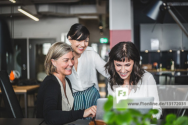Creative businesswomen smiling while discussing over laptop at desk in office