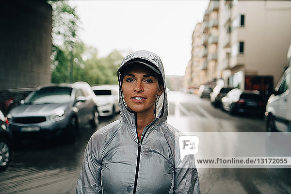 Porträt einer selbstbewussten Sportlerin in nasser Kapuzenjacke  die in der Stadt auf der Straße steht