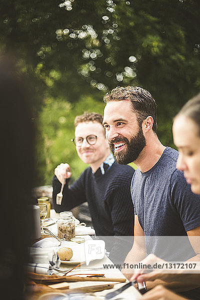 Lächelnder Mann schaut weg  während er eine Dinnerparty mit Freunden im Hinterhof genießt