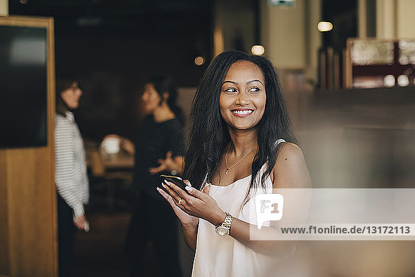 Smiling young businesswoman using smart phone in office