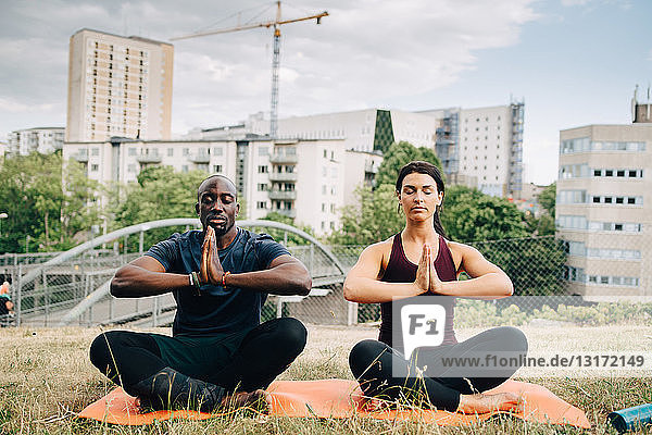 Multi-ethnische Freunde praktizieren Yoga auf dem Feld gegen Gebäude in der Stadt