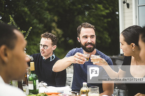 Man and woman toasting drinks while enjoying dinner party with friends in backyard