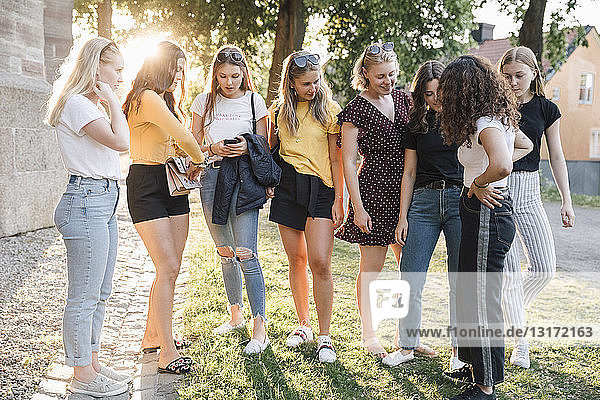 Full length of female friends standing on grass at park during sunny day