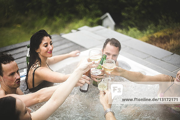 Carefree male and female friends toasting drinks in hot tub during weekend getaway