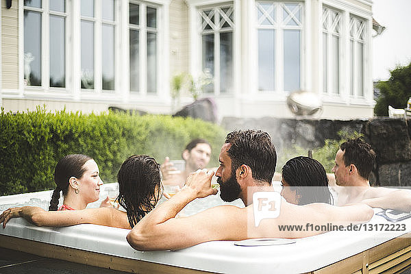 Mid adult man drinking alcohol while enjoying with friends in hot tub during weekend