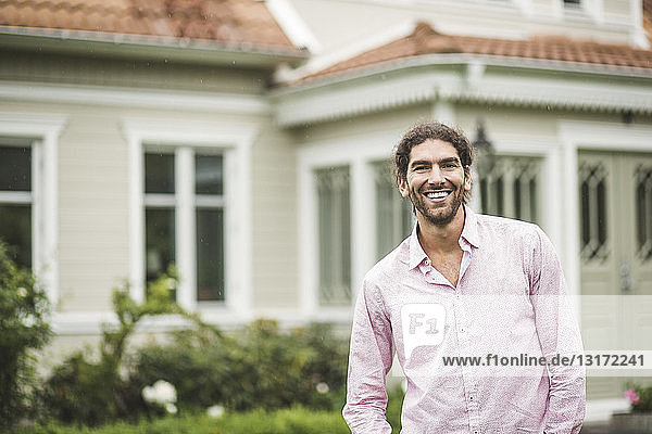 Porträt eines fröhlichen jungen Mannes  der vor einer Villa steht