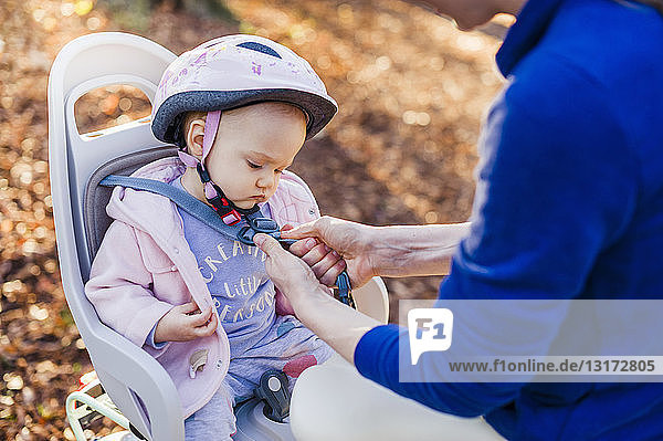 Mutter und Tochter fahren Fahrrad,  das Baby trägt einen Helm und sitzt im Kindersitz