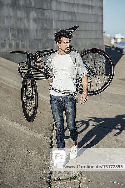 Young man carrying commuter fixie bike at concrete wall