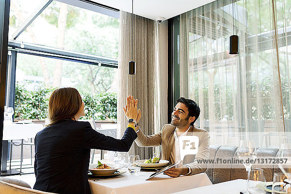 Happy man and woman with a tablet in a restaurant high fiving