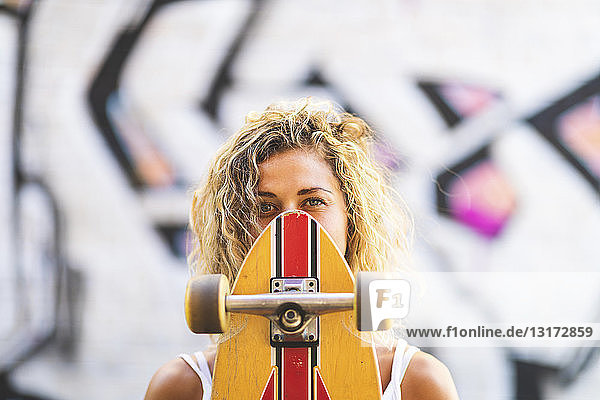 Porträt einer jungen Frau mit Skateboard an einer Graffiti-Wand
