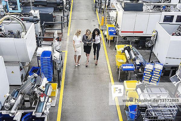 Three women with tablet walking and talking in factory shop floor