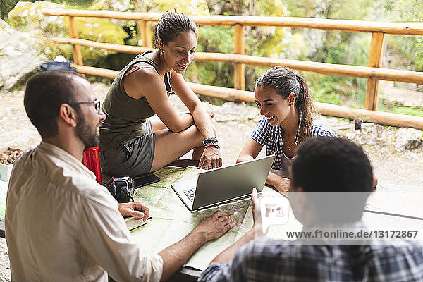 Group of hikers sitting together planning a hiking route using map and laptop