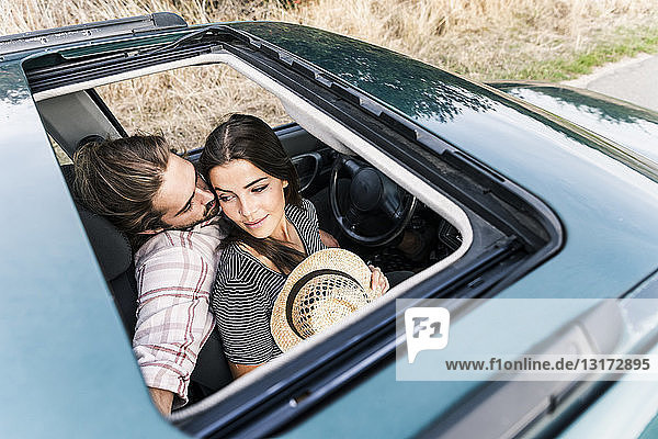 Zärtliches junges Paar in einem Auto durch das Schiebedach gesehen