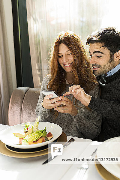 Glückliches Paar benutzt Handy in einem Restaurant