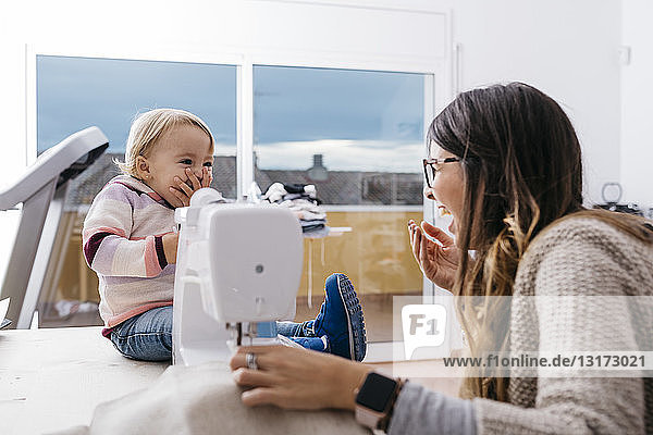 Glückliche Mutter mit kleiner Tochter zu Hause mit Nähmaschine