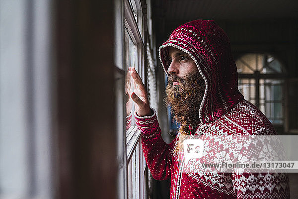 Portrait of pensive man with beard wearing hooded jacket looking out of window
